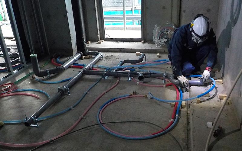 床に配管を組む狩野設備工業の作業員。配管工事の様子